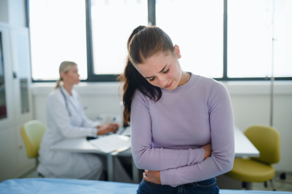 Teenage girl with the stomach ache sitting in doctor's office.