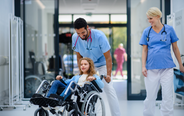 Young multiracial doctor having fun with little girl on a wheelchair.