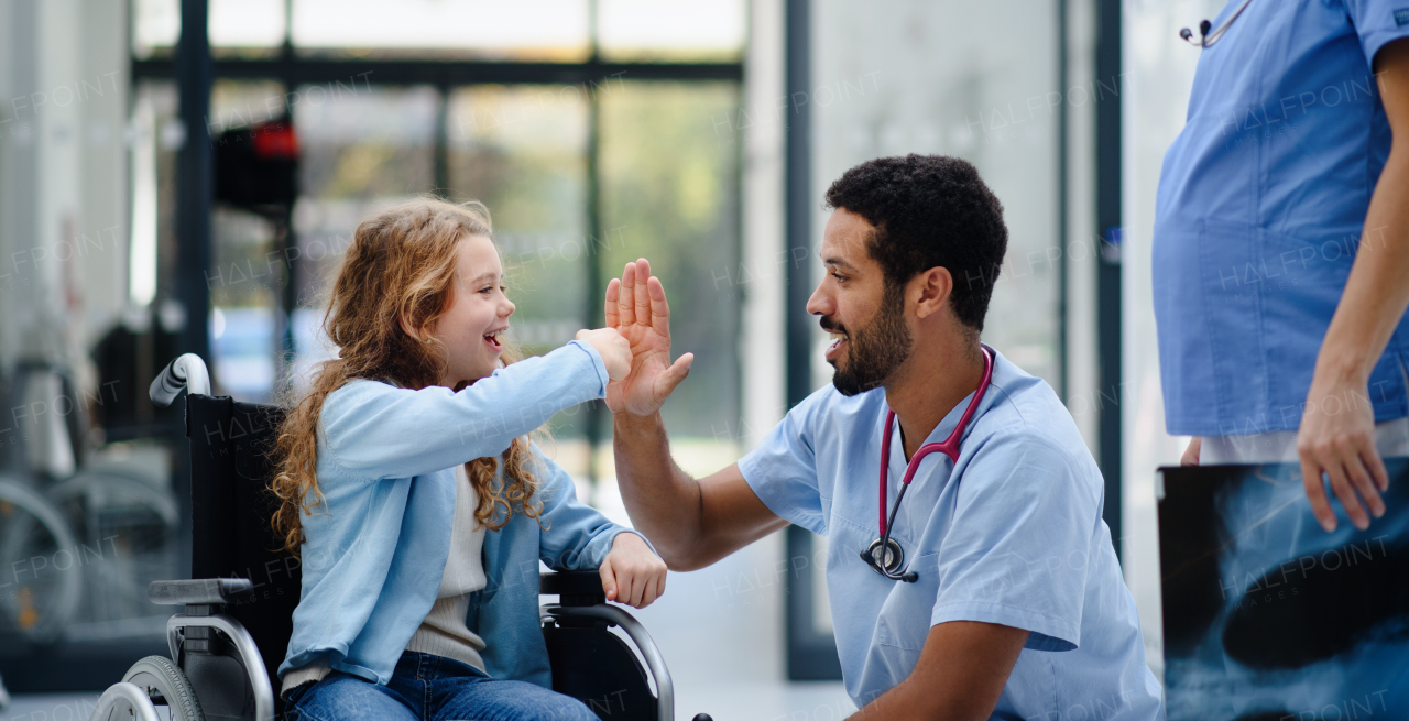 Young multiracial doctor having fun with little girl on a wheelchair.