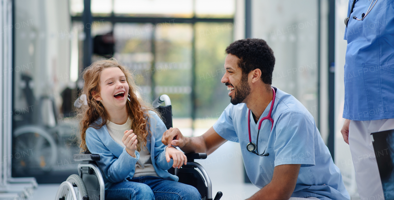 Young multiracial doctor having fun with little girl on a wheelchair.