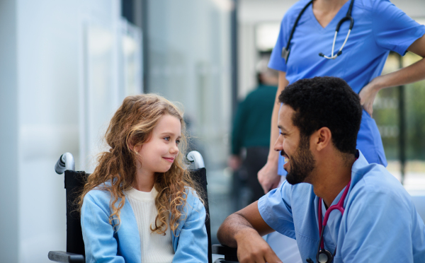 Young multiracial doctor talking with little girl on a wheelchair.