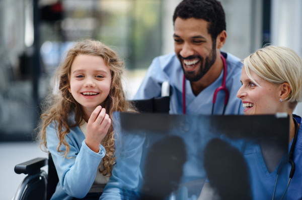 Young multiracial doctor with his colleague showing x-ray image of lungs to little patient on wheelchair.