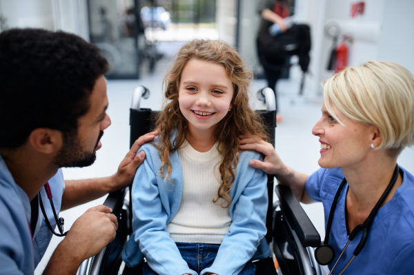 Young multiracial doctor and his colleague talking with little girl on a wheelchair.