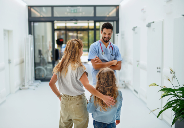 Young multiracial doctor talking with mother of little girl at a hospital corridor.