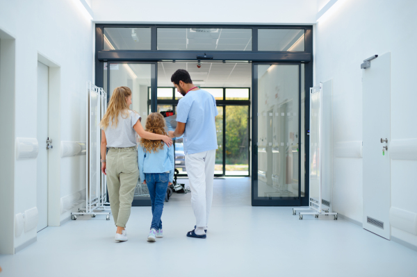 Rear view of young multiracial doctor talking with mother and little girl at hospital corridor,showing them a x-ray image.