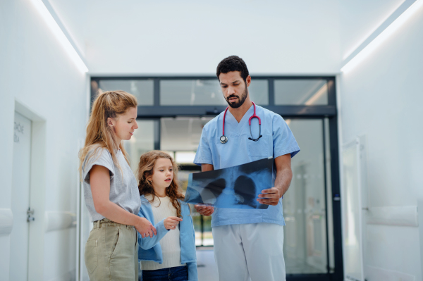 Young multiracial doctor talking with mother of little girl at a hospital corridor.