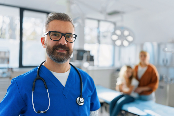 Portrait of mature doctor in a surgery room, mother with child in background.