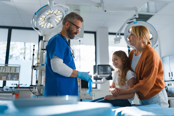 Mature doctor giving gypsum to little girl on her broken arm.