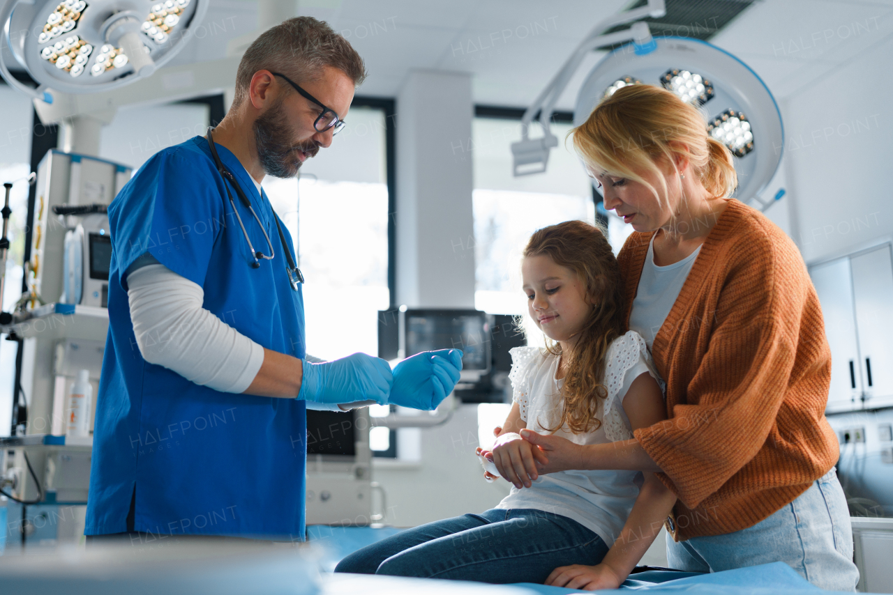 Mature doctor giving gypsum to little girl on her broken arm.