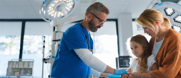 Mature doctor giving gypsum to little girl on her broken arm.