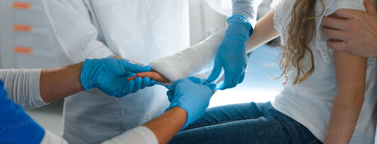 Close-up of doctor giving gypsum to little girl on her broken arm.