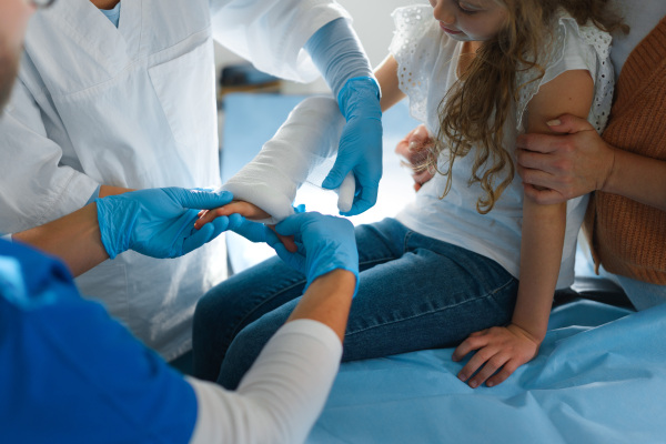 Close-up of doctor giving gypsum to little girl on her broken arm.