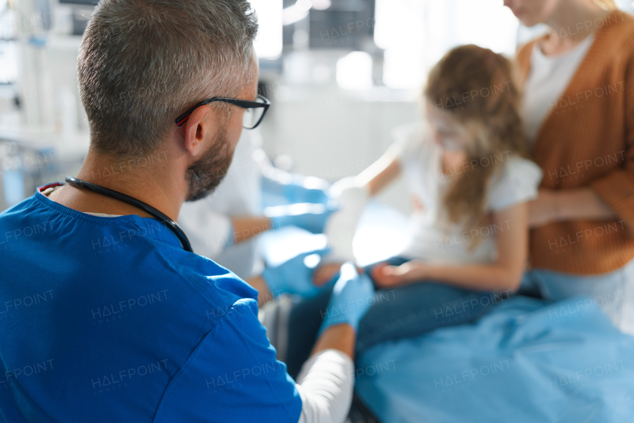 Mature doctor giving gypsum to little girl on her broken arm.