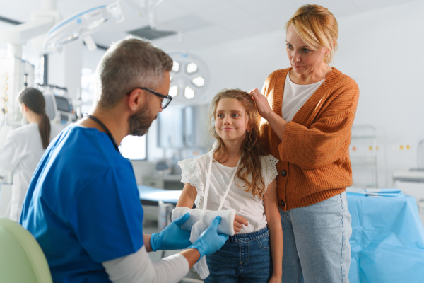 Mature doctor giving gypsum to little girl on her broken arm.