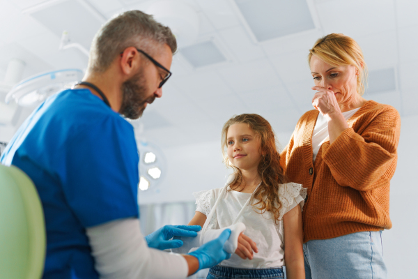 Mature doctor giving gypsum to little girl on her broken arm.