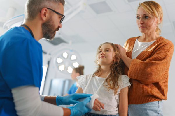 Mature doctor giving gypsum to little girl on her broken arm.