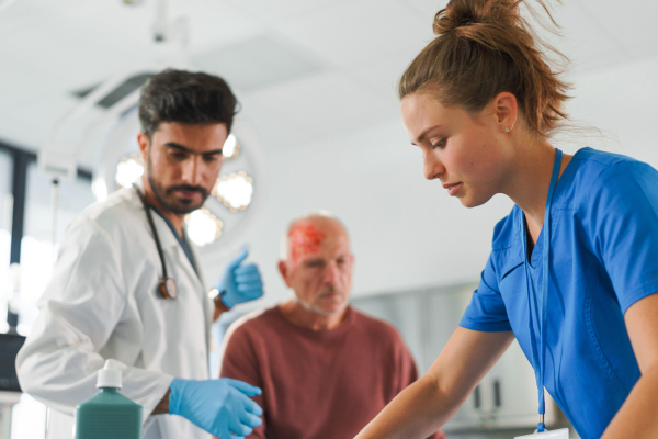 Young doctor and nurse treating injured head of senior man.