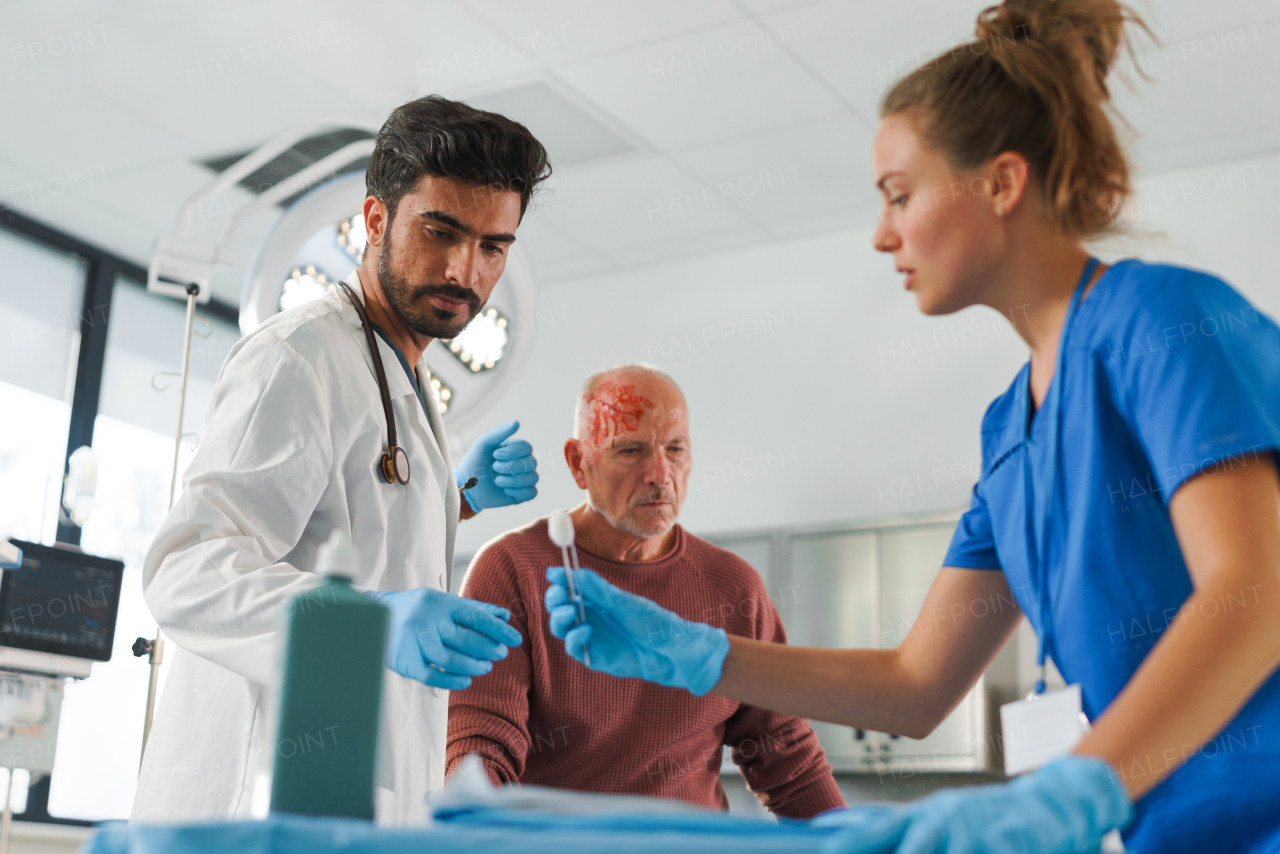 Young doctor and nurse treating injured head of senior man.