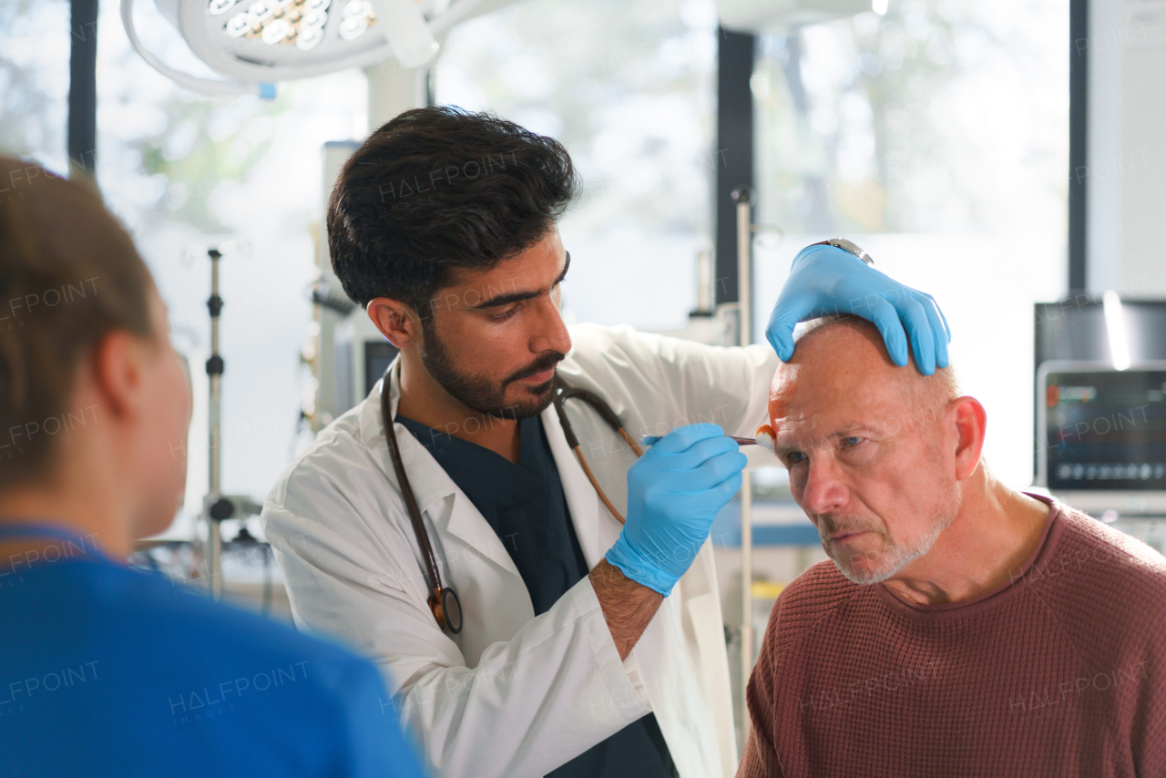 Close-up of doctor and nurse treating injured head of senior man.