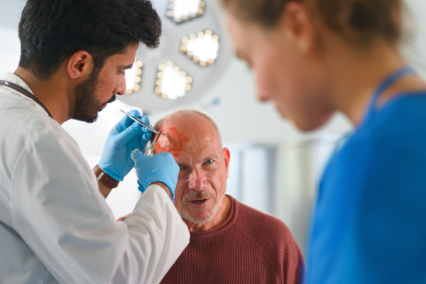 Close-up of doctor and nurse treating injured head of senior man.