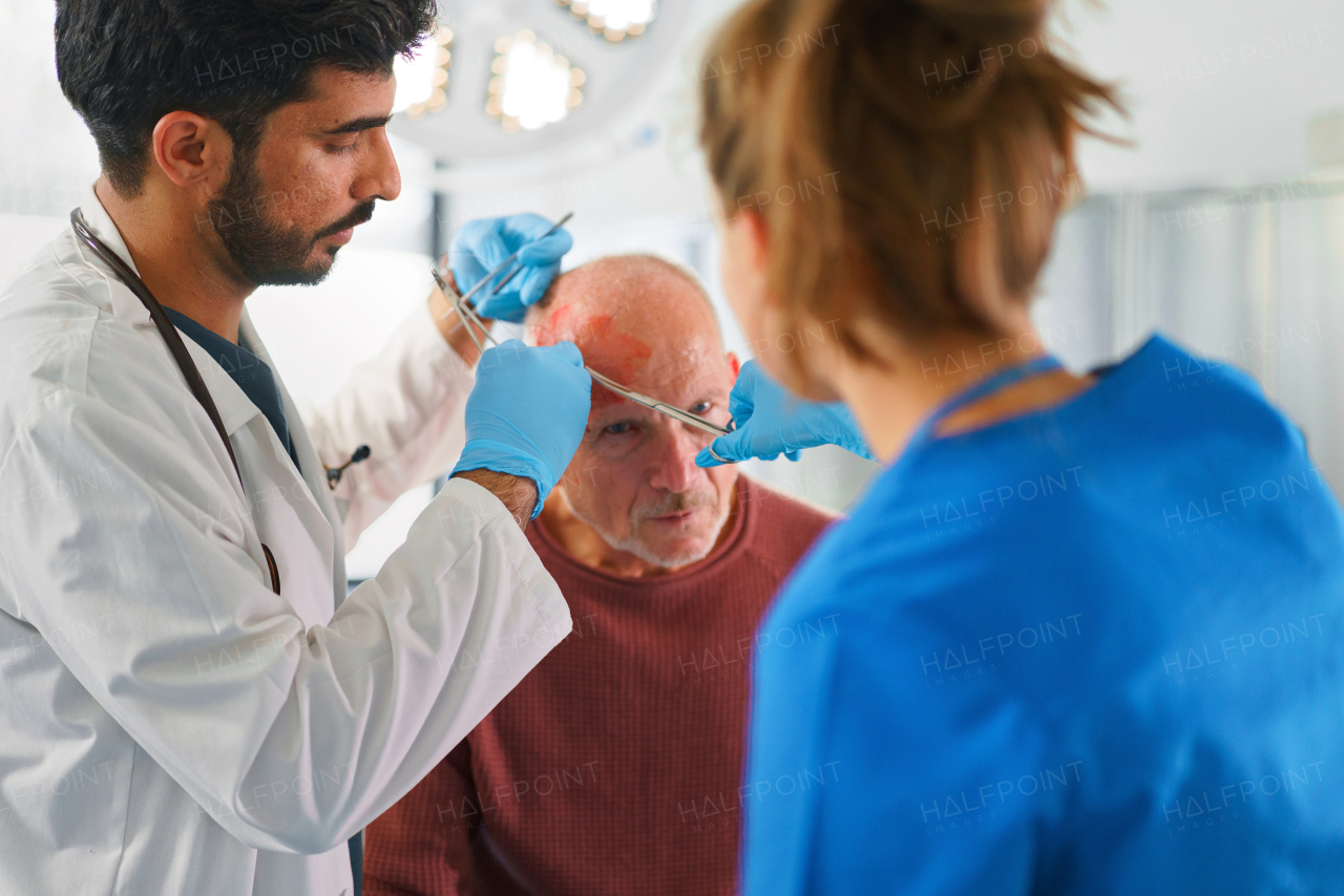 Young doctor and nurse treating injured head of senior man.