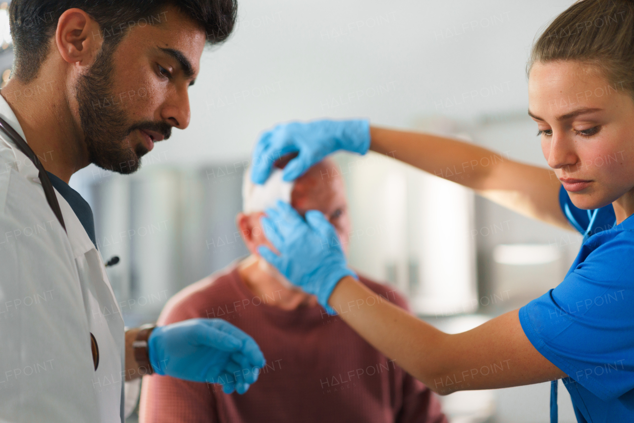 Young doctor and nurse treating injured head of senior man.