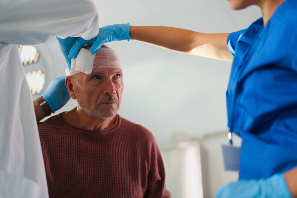 Close-up of doctor and nurse treating injured head of senior man.