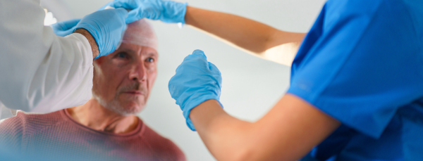 Close-up of doctor and nurse treating injured head of senior man.