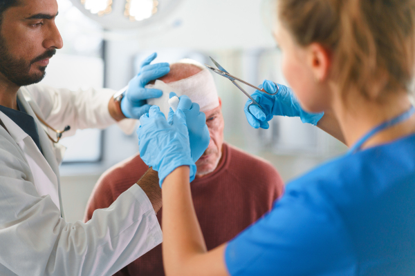 Close-up of doctor and nurse treating injured head of senior man.