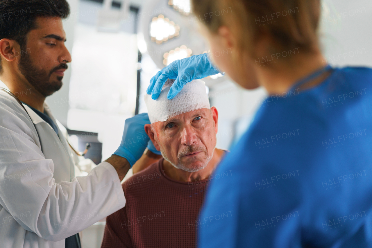 Young doctor and nurse treating injured head of senior man.