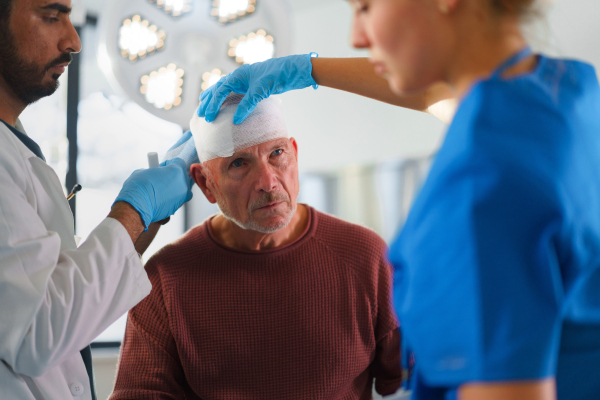 Close-up of doctor and nurse treating injured head of senior man.