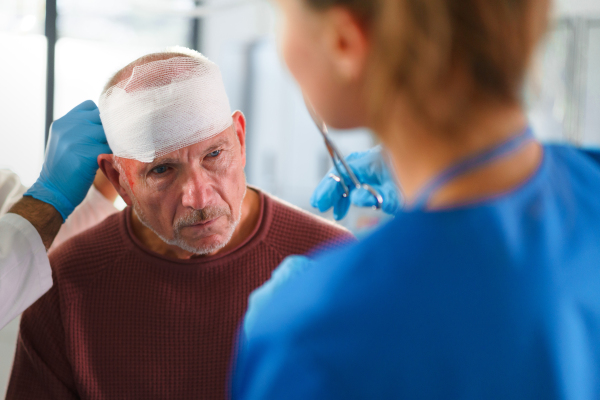 Close-up of doctor and nurse treating injured head of senior man.