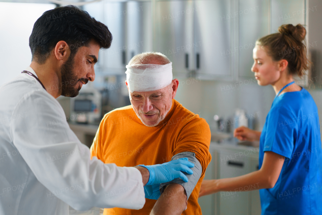 Young doctor and nurse treating injured head of senior man.