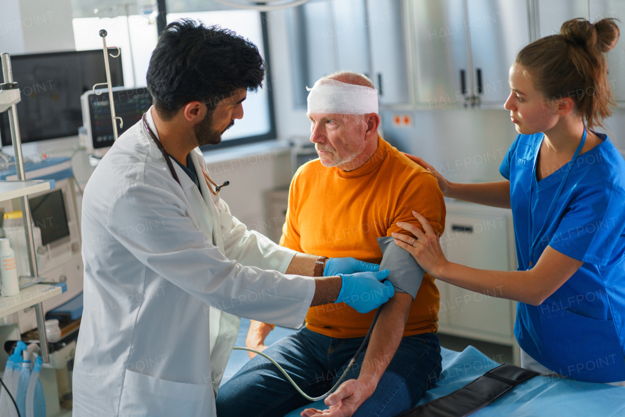 Young doctor and nurse treating injured head of senior man.