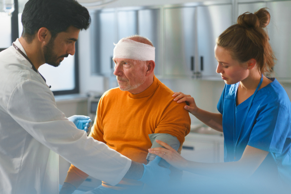 Young doctor and nurse treating injured head of senior man.