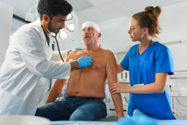 Young doctor and nurse treating injured head of senior man.