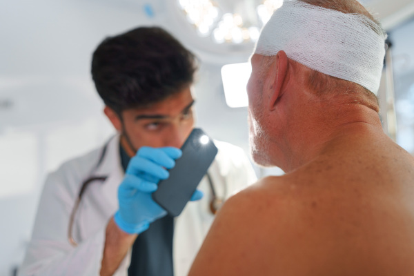 Doctor examining senior man with injured head.