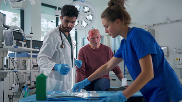 Young doctor and nurse treating injured head of senior man.