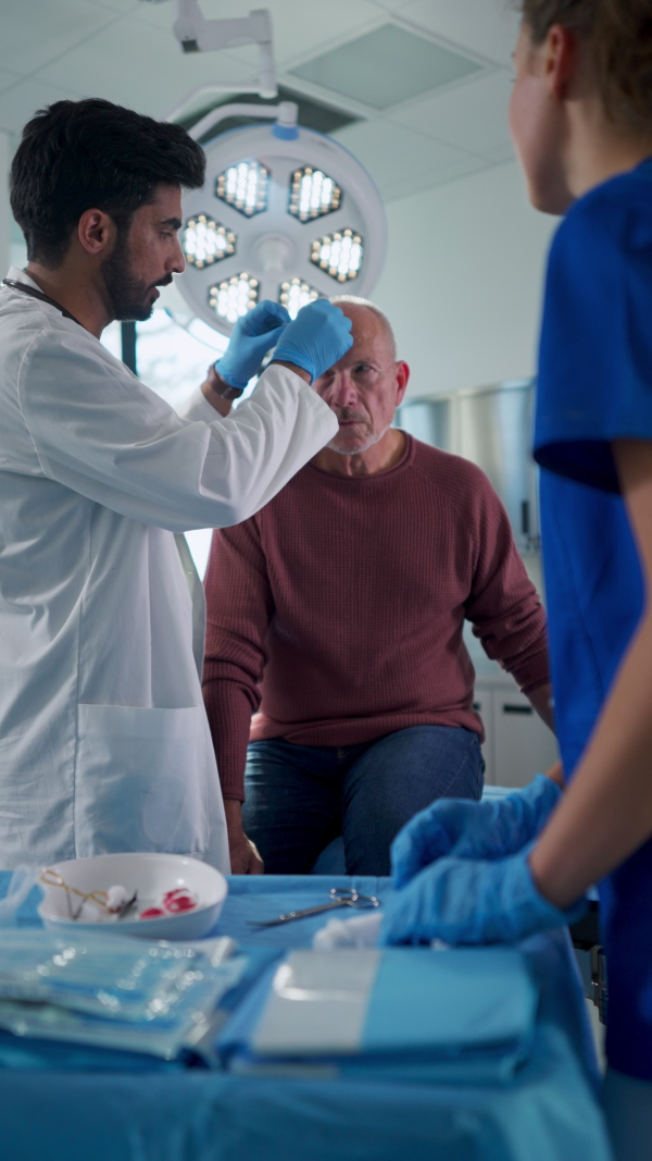 Young doctor and nurse treating injured head of senior man. Vertical view.