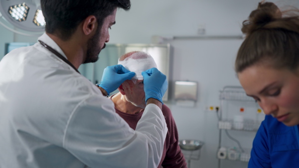 Young doctor and nurse treating injured head of senior man.