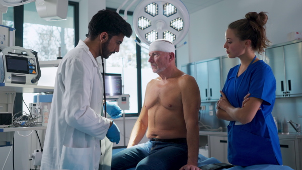 Young doctor and nurse treating injured head of senior man.