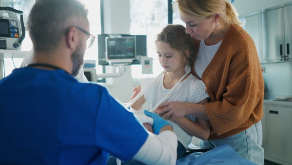 Mature doctor giving gypsum to little girl on her broken arm.