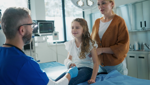 Mature doctor giving gypsum to little girl on her broken arm.