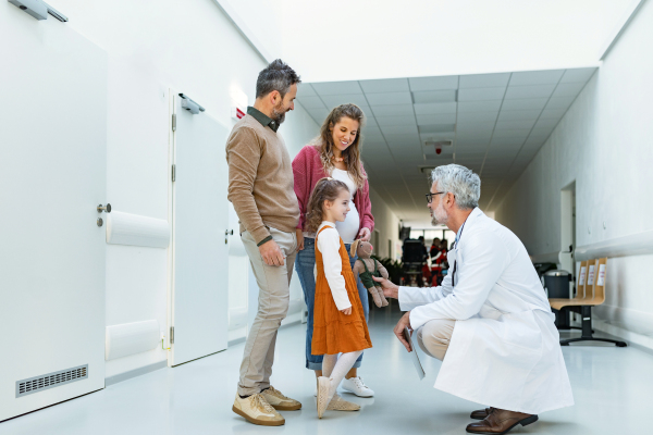 Pediatrician looking at girl's toy. Girl patient is at examination in a modern clinic with her parents. Emotional support during medical examination in hospital.