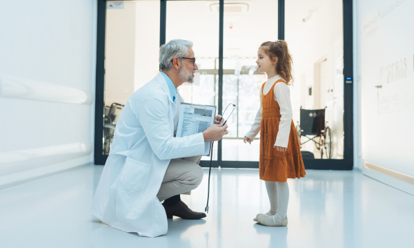 Little girl talking with doctor in hospital lobby. Friendly relationship between healthcare workers and the child patient.