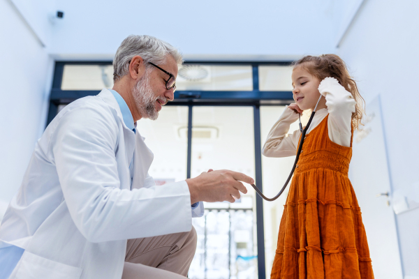 Little girl listening to the doctor's heart with stethoscope. Role reversal. Friendly relationship between the doctor and the child patient.