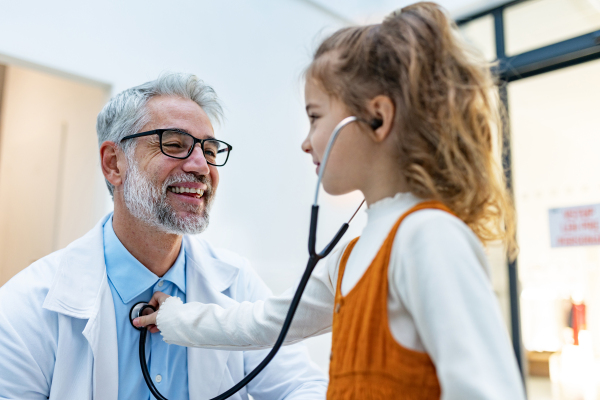 Little girl listening to the doctor's heart beat with stethoscope. Role reversal. Friendly relationship between the doctor and the child patient.