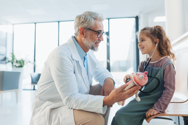 Little girl listening to the plush toy's heartbeat with stethoscope. Role reversal. Friendly relationship between the doctor and child patient. Emotional support for children.