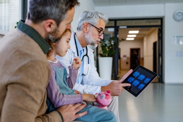 Doctor explaining results of MRI scan of brain to father of young girl patient. Diagnosis of diseases and head injuries. Concept of children healthcare and emotional support for child patients.