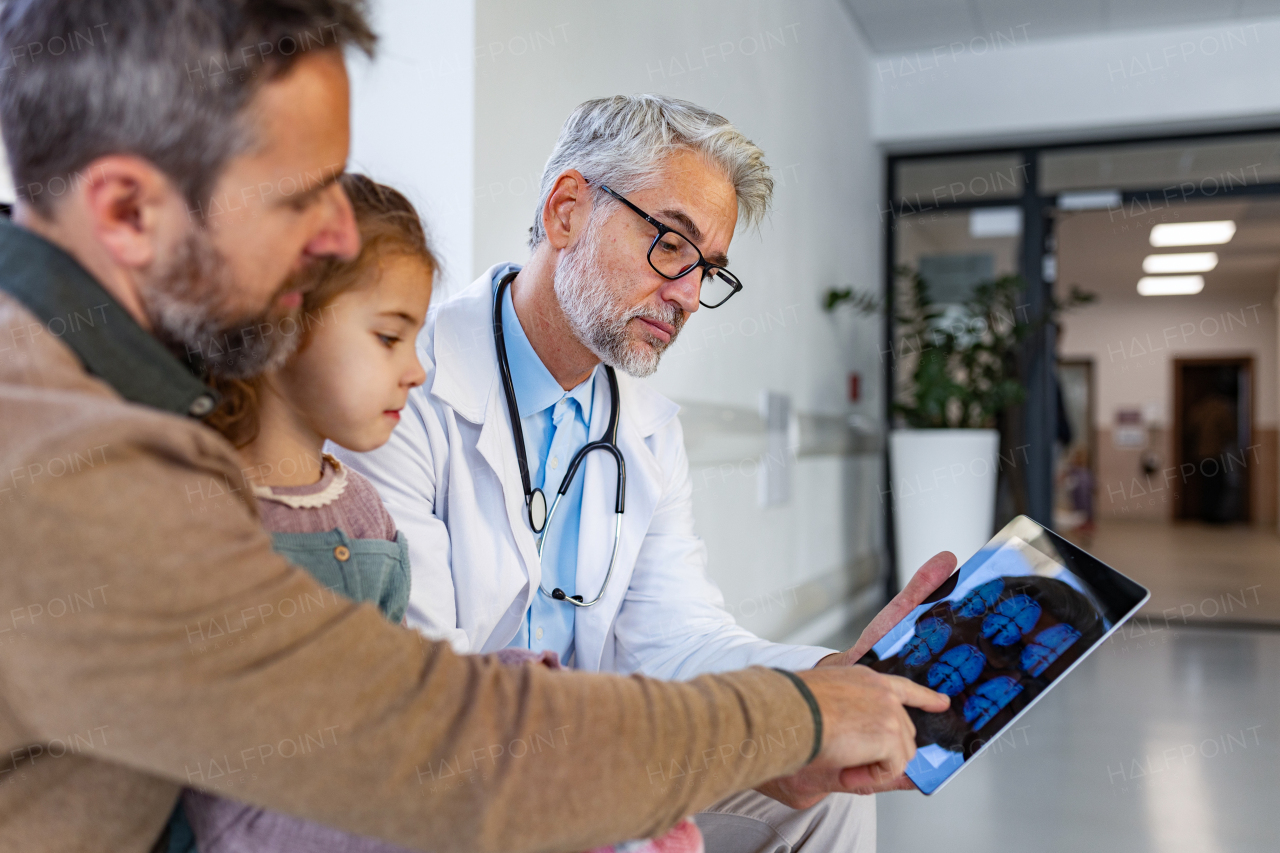 Doctor explaining results of MRI scan of brain to father of young girl patient. Diagnosis of diseases and head injuries. Concept of children healthcare and emotional support for child patients.